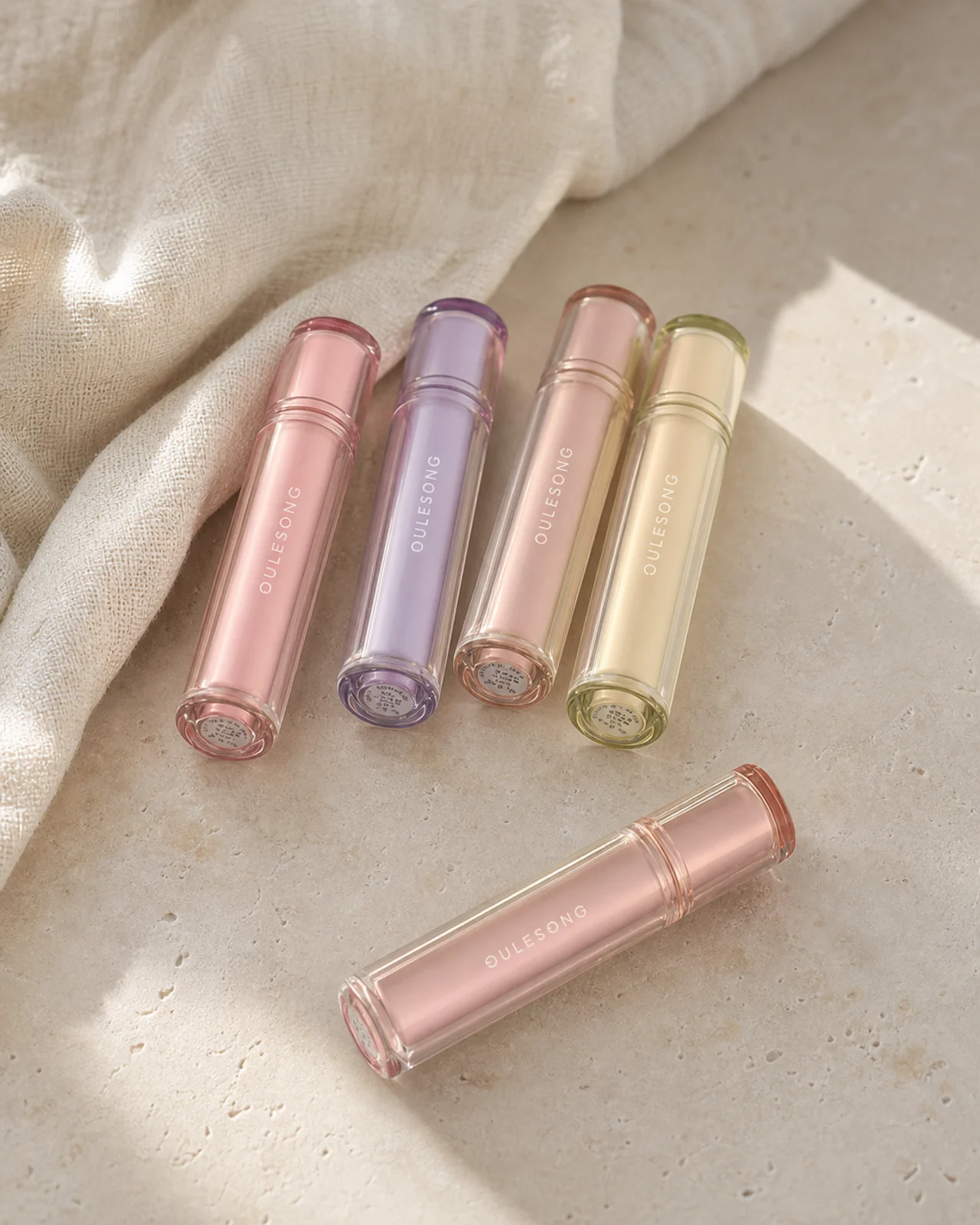 Five pastel lip tints arranged on a warm stone table in natural light