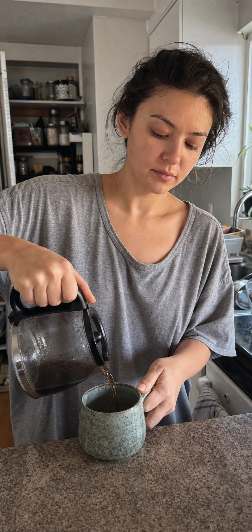 A woman wearing a single round pimple patch on her chin pours coffee in a small home kitchen.
