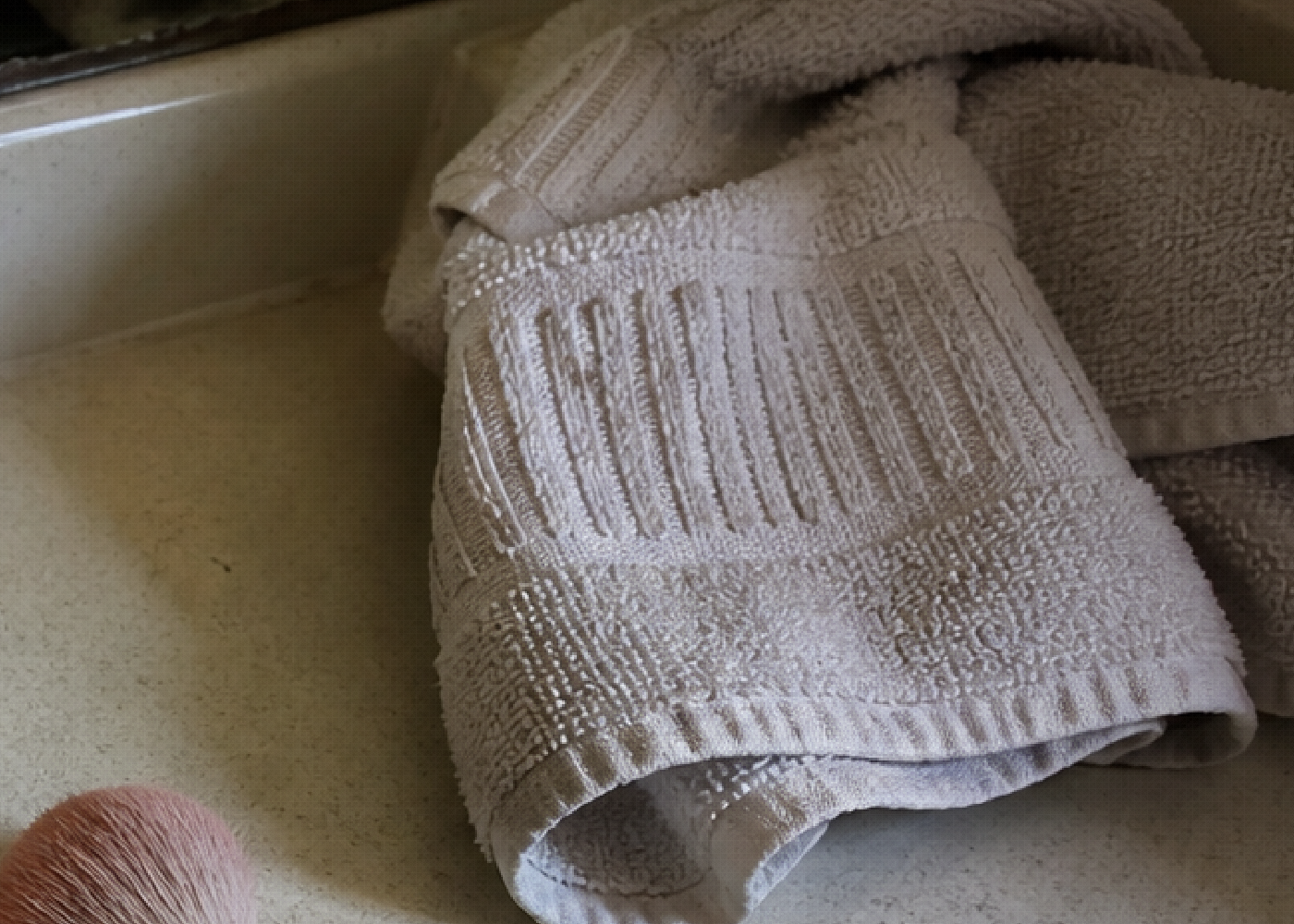 A folded towel rests on a bathroom counter beside the sink in warm light.