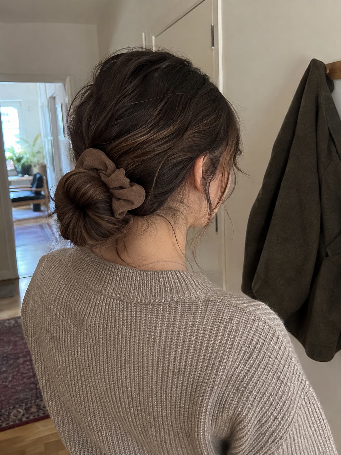 A relaxed low bun held with a brown fabric scrunchie, with loose strands around the nape.